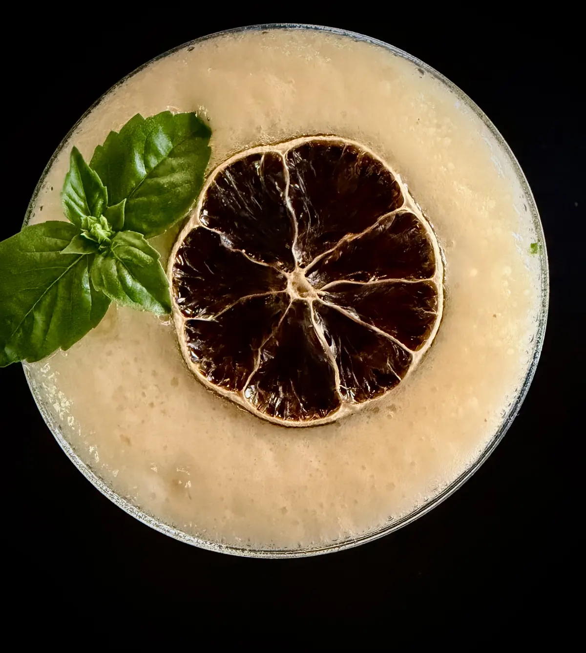 Un cocktail con schiuma, basilico e limone essiccato, visto dall’alto