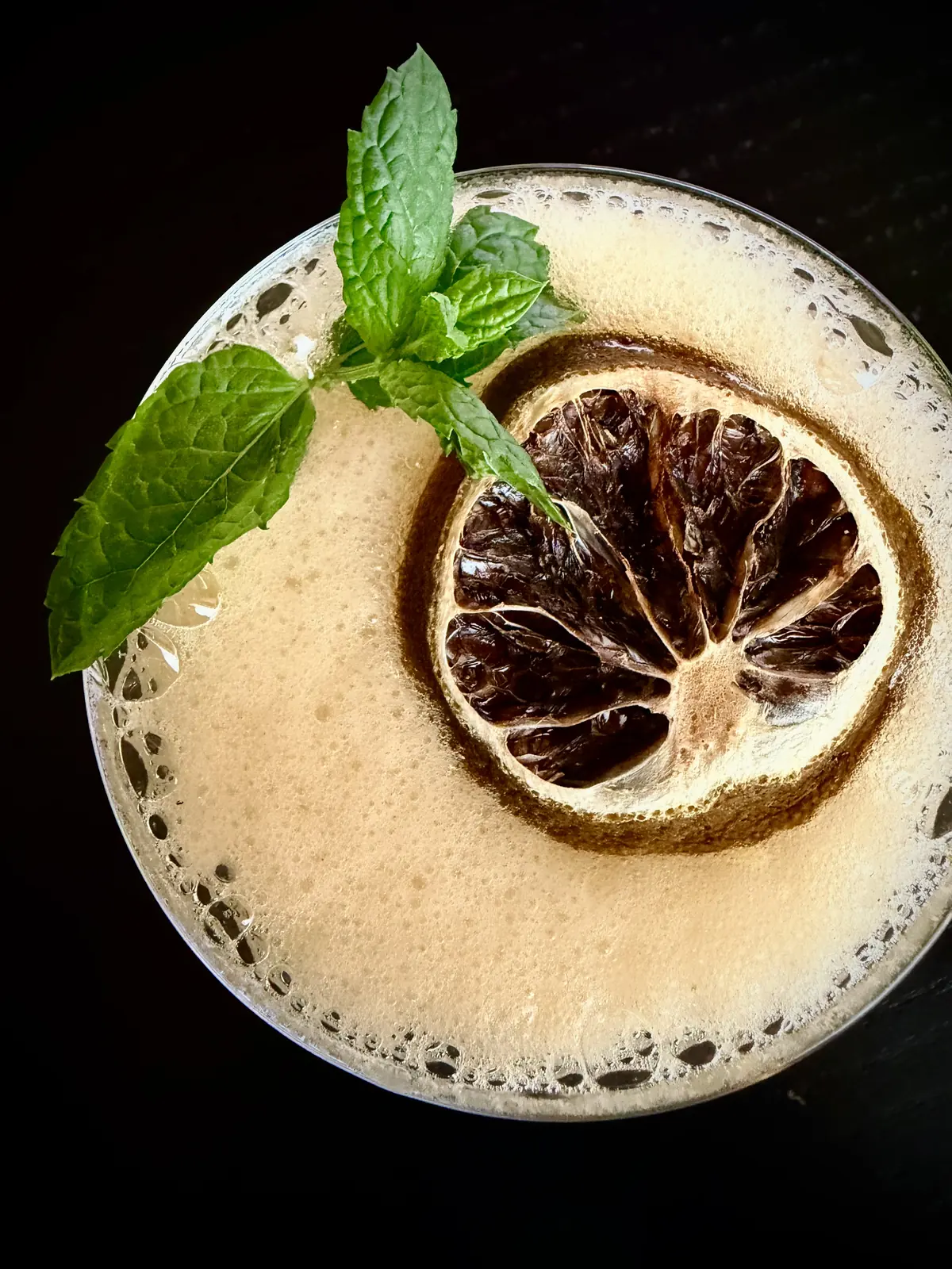 Un cocktail con schiuma, menta e una fetta di limone essiccato, visto dall’alto