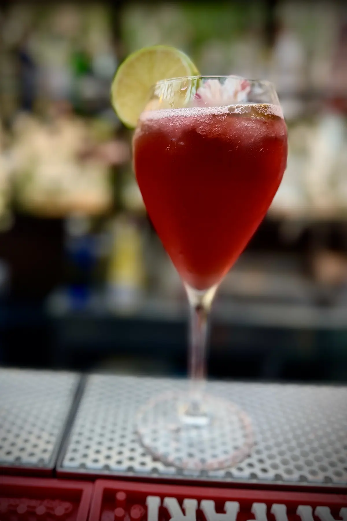 Un cocktail rosso nel calice con una fetta di lime, sul bancone