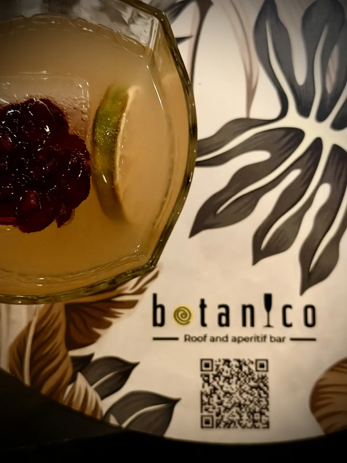 Un cocktail con frutti rossi e lime sulla tovaglietta a foglie di Botanico