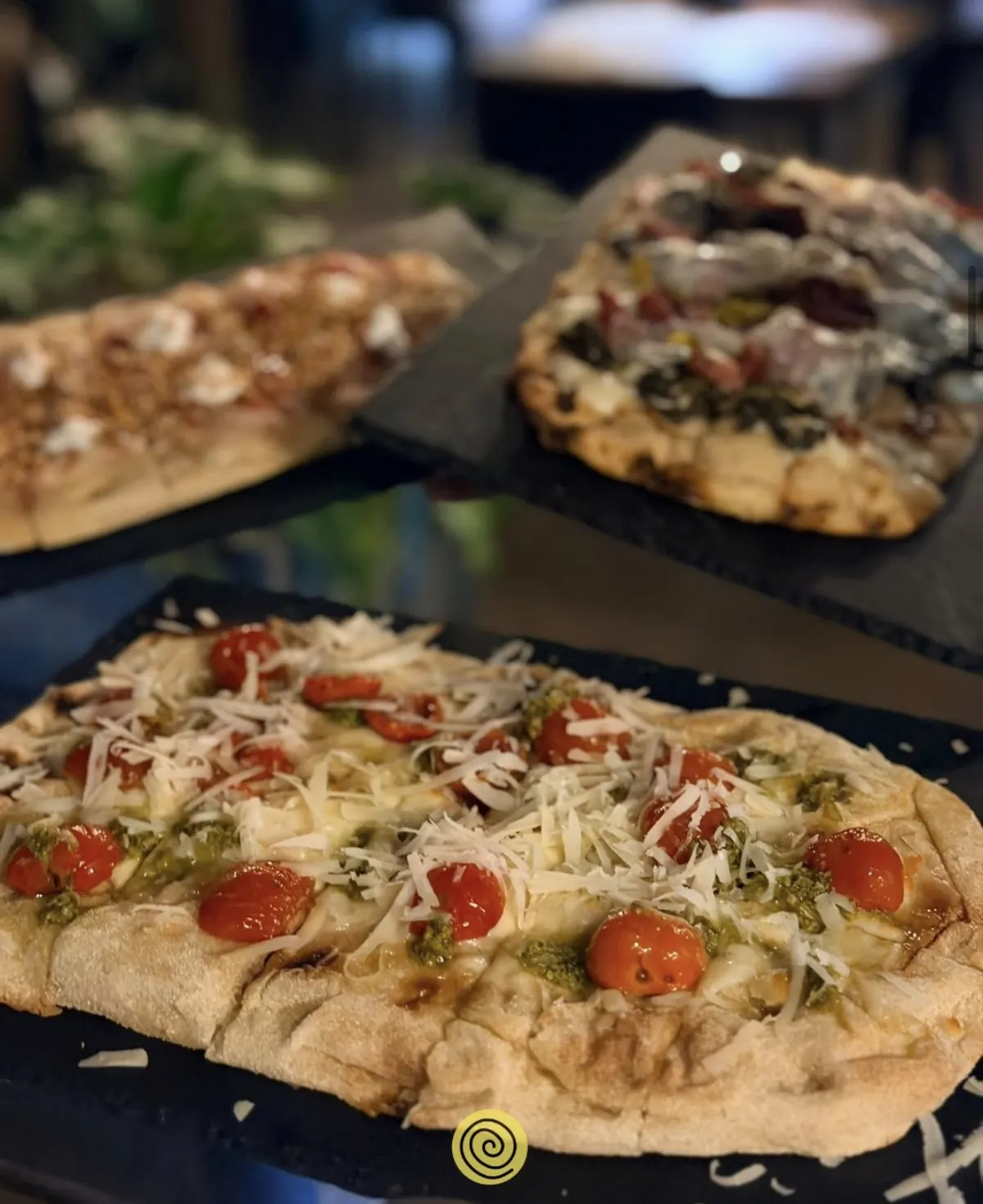 Pinse su ardesia: in primo piano pomodorini, pesto e scaglie di grana